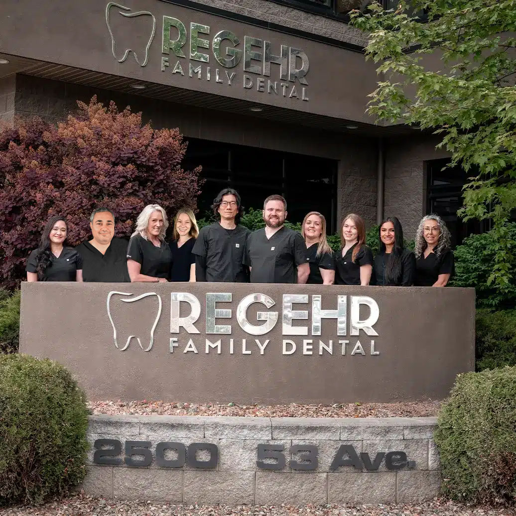 Regehr Family Dental team standing behind the sign in front of their Vernon Dental clinic
